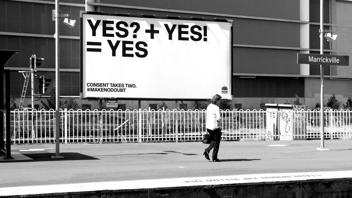 Person walking in front of YES campaign billboard at train station
