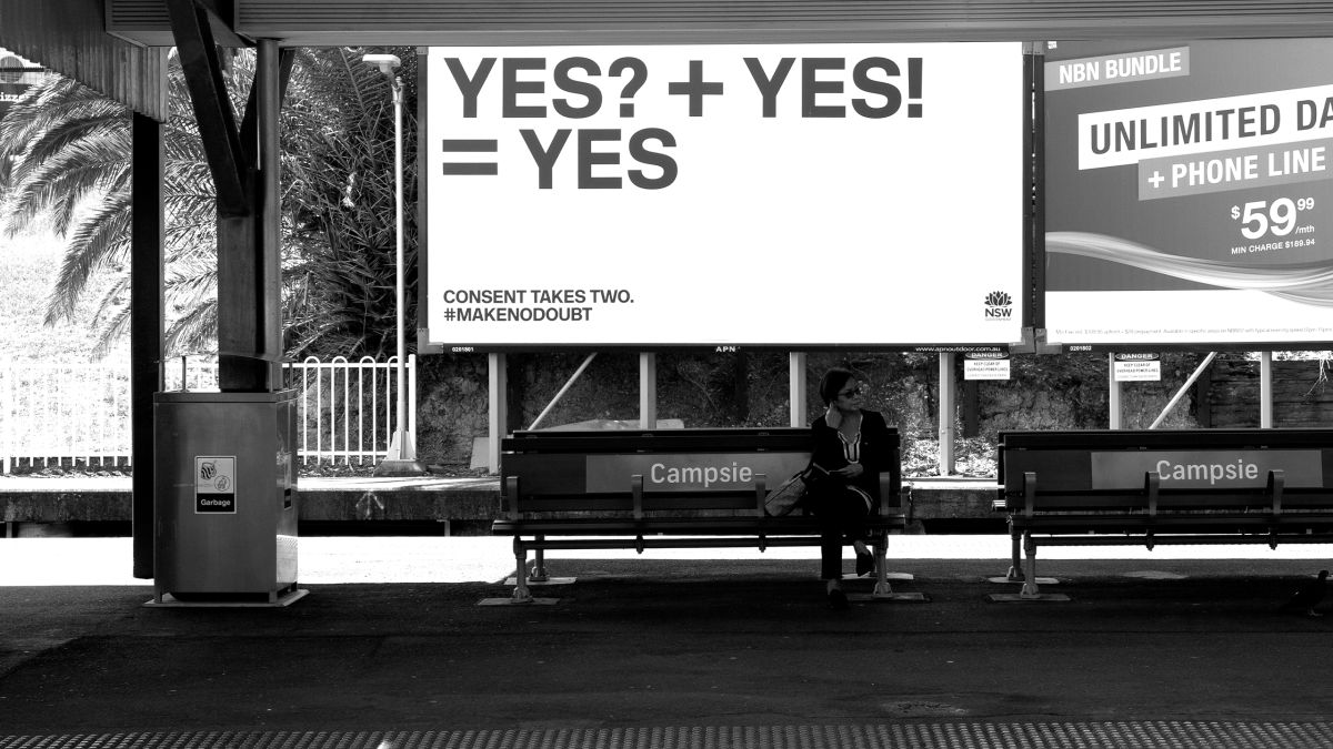 Woman sitting in front of YES campaign billboard at train station
